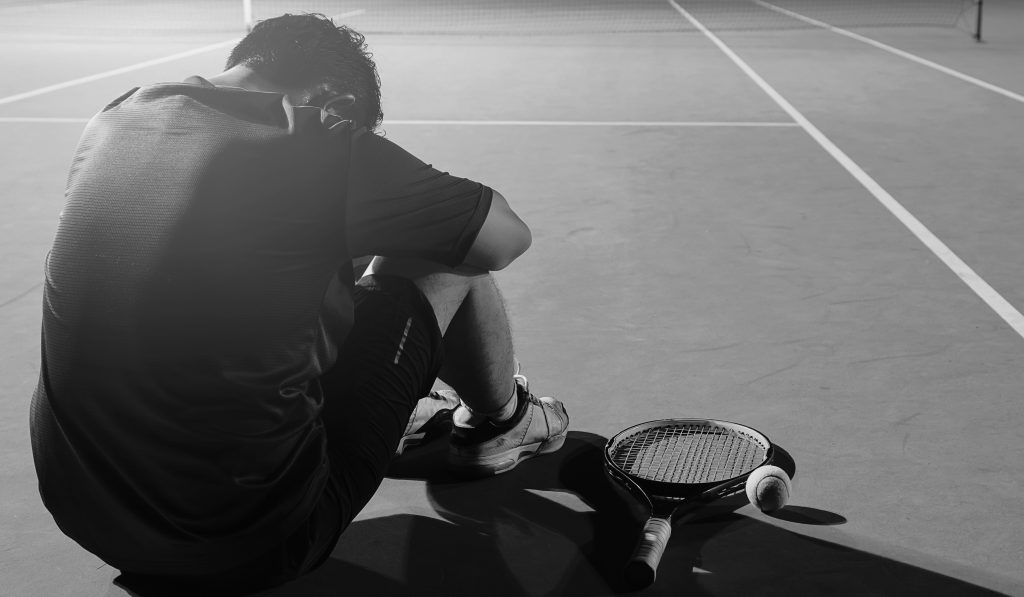 Sad tennis player sitting in the court after lose a match