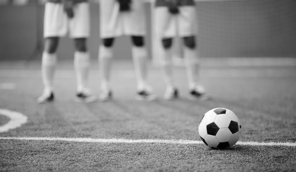 Soccer ball on green football field by dividing line and legs of three players on background