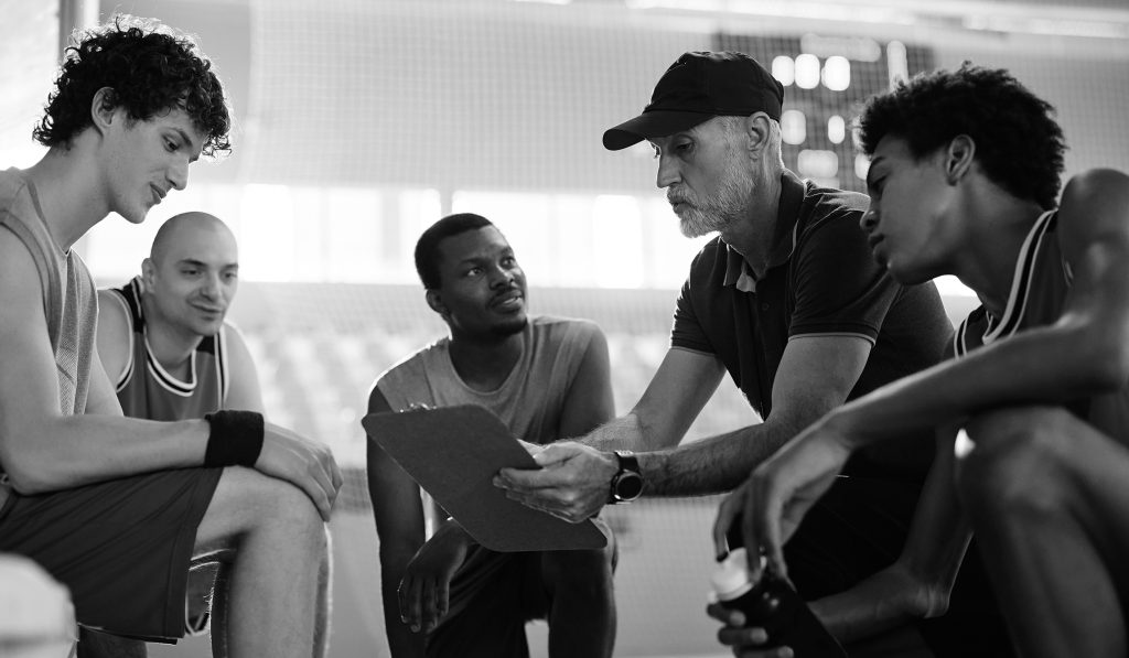 Team of basketball players listening to their coach while his is talking about game strategy during sports training.
