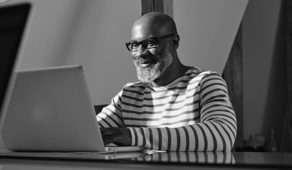 Portrait of smiling man sitting at his desk working with laptop