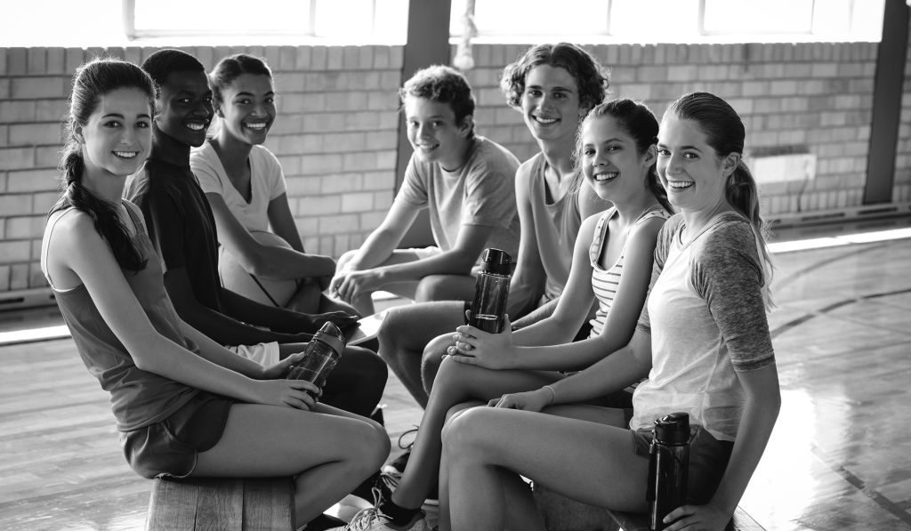 Portrait of smiling high school kids relaxing in basketball court