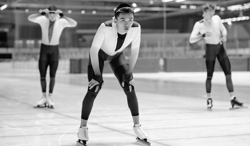 Young male athlete in sportive uniform ready to move forwards waiting for signal to start while standing on skating rink during training